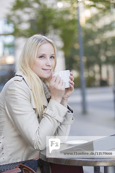 Hübsche blonde Frau genießt eine Tasse Kaffee in der Innenstadt.