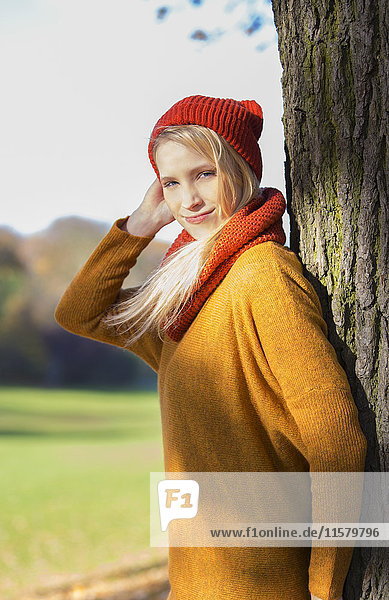 Blonde Frau lehnt sich im Herbst an einen Baum im Park.