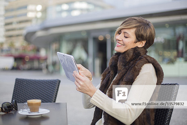 Frau lächelt mit Tablette in einem Cafe im Freien