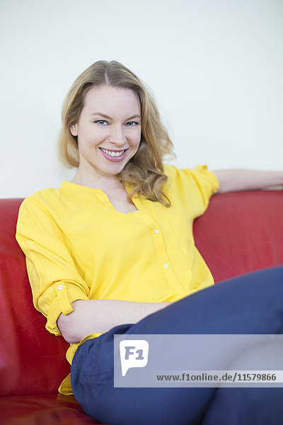 Porträt einer hübschen blonden Frau auf der Couch  die vor der Kamera lächelt.