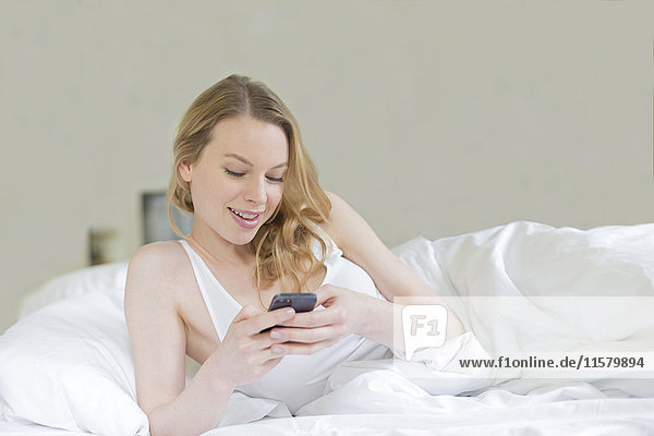 Content pretty blonde woman with mobile in bed