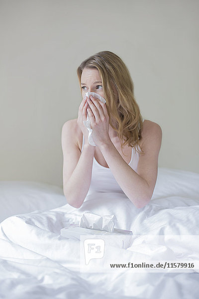 Frau krank mit Taschentüchern im Bett