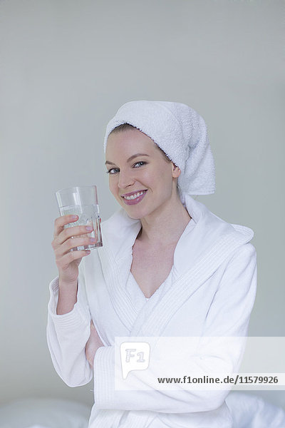 Frau im Bademantel mit einem Glas Wasser lächelnd vor der Kamera