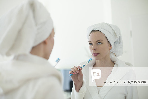 Woman in bathrobe brushing her teeth in front of the mirror