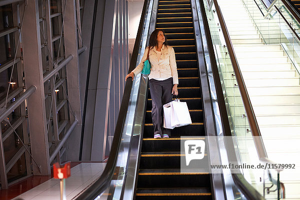 Reife Frau mit Einkaufstüten  die sich auf der Rolltreppe in einem Einkaufszentrum nach unten bewegen  Dubai  Vereinigte Arabische Emirate