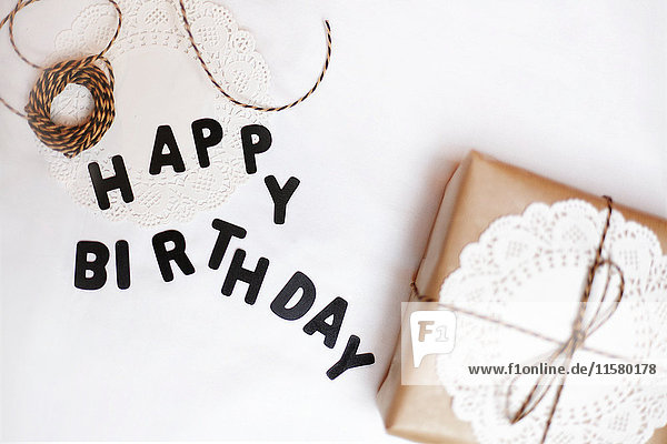Geschenk verpackt in braunes Papier  Deckchen und Schnur  daneben Buchstaben mit der Aufschrift Happy Birthday