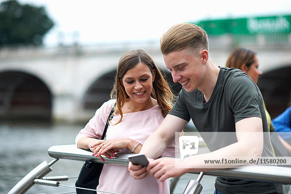 Young man and woman beside river  looking at smartphone