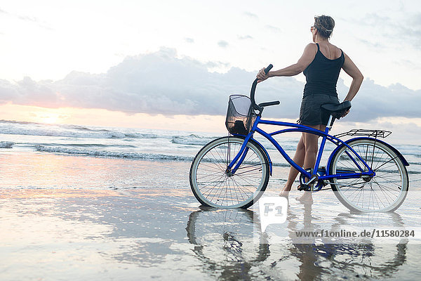Frau mit Fahrrad  die bei Sonnenuntergang vom Strand hinausschaut  Nosara  Provinz Guanacaste  Costa Rica