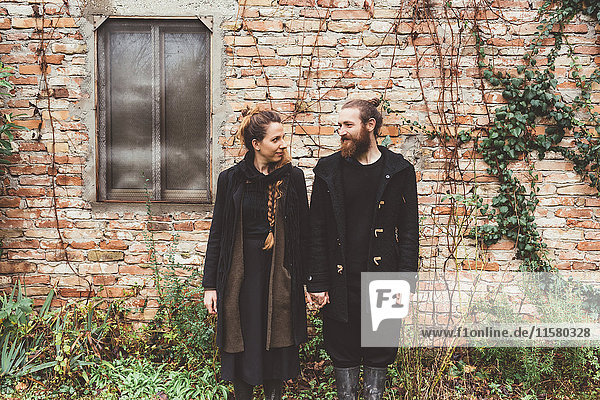 Porträt eines Paar  das sich an einem Nebengebäude an der Hand hält
