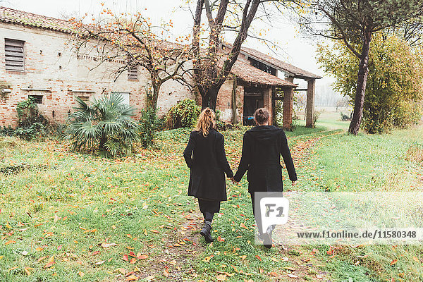Rückansicht eines Paares beim Spaziergang durch alte landwirtschaftliche Gebäude