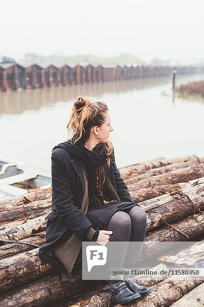Junge Frau sitzt auf Baumstämmen am Ufer des nebligen Kanals