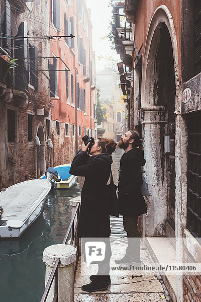 Couple photographing building exteriors from canal waterfront  Venice  Italy