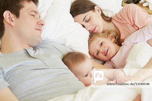 Baby girl and toddler sister huddled in bed with sleeping parents
