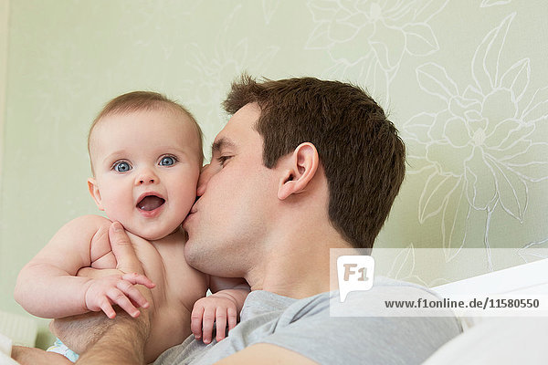 Mid adult man kissing baby daughter on cheek in bed