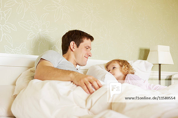 Weibliches Kleinkind und Vater starren sich im Bett an