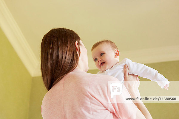 Low angle view of mid adult woman holding baby daughter in bedroom