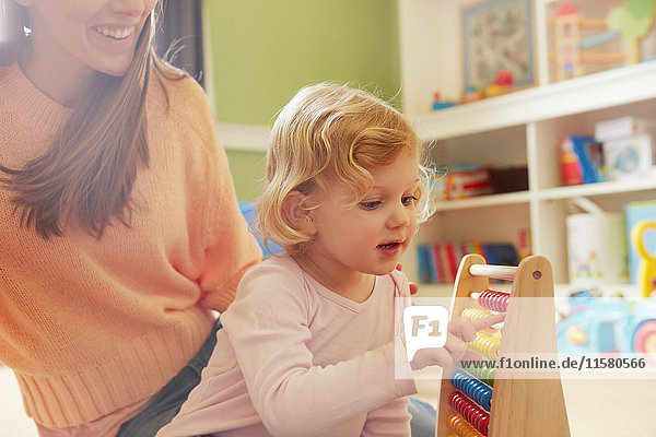 Mid adult woman and toddler daughter counting on abacus in playroom