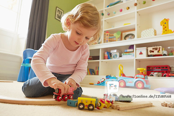 Female toddler playing with toy train on playroom floor