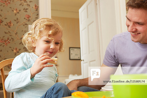 Mid adult man and toddler daughter eating bread at kitchen table