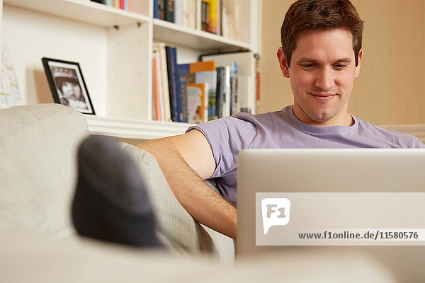Mid adult man sitting on sofa looking at laptop