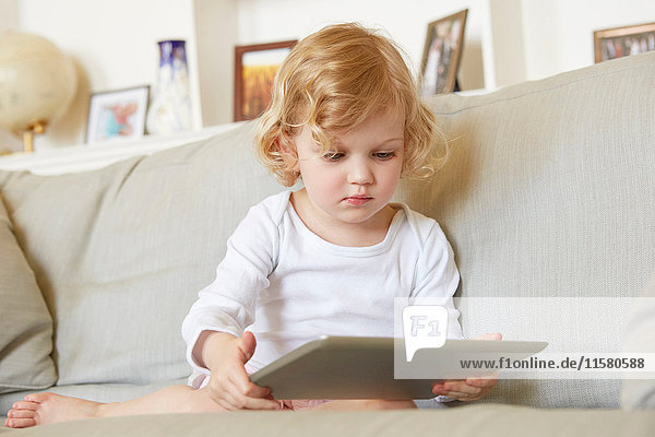 Female toddler sitting on sofa using digital tablet
