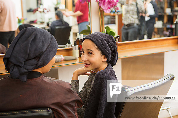 Girl and mother with towels on heads chatting in hair salon