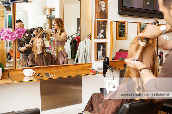 Friseure mit Lockenstab auf Kunden lange rote Haare im Salon