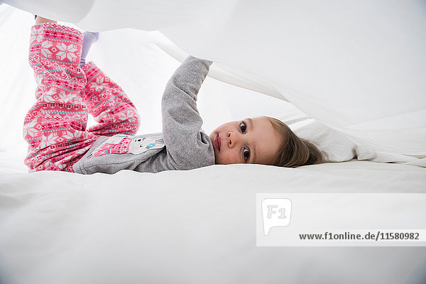 Porträt eines weiblichen Kleinkindes zwischen weißen Bettlaken liegend