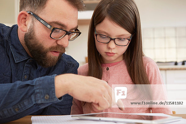 Mittelgroßer erwachsener Mann erklärt der Tochter bei Tisch Hausaufgaben