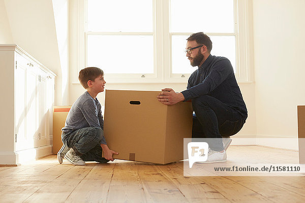 Mittlerer Erwachsener Mann und Sohn kauernd  um den Karton in ein neues Zuhause zu heben.