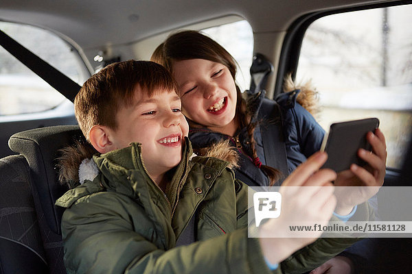 Boy and sister taking laughing selfie in car backseat