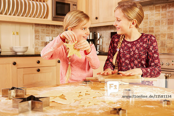 Two girls baking star shape pastry at kitchen table