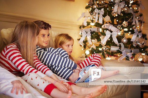 Boy and girls in striped pyjamas on sofa at christmas