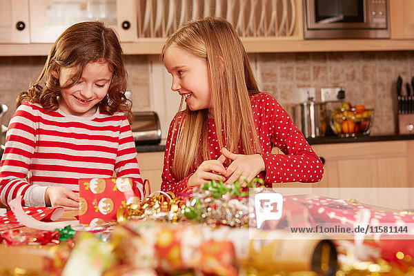 Two girls wrapping christmas presents at table