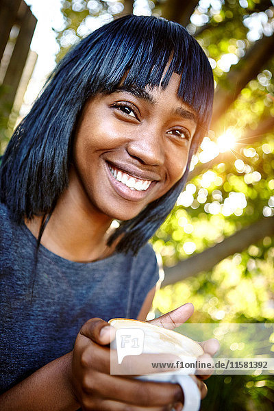 Porträt einer jungen Frau  die im Freien sitzt  eine Kaffeetasse hält und lächelt