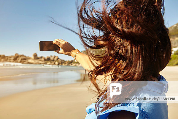 Reife Frau am Strand  Selfie  Smartphone benutzen  Rückansicht