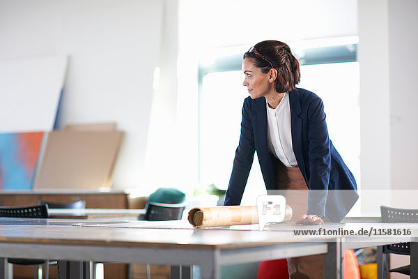 Woman in office leaning against desk looking away
