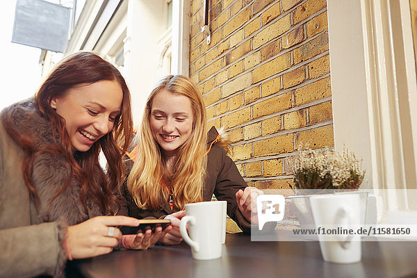 Zwei Freundinnen  die im Freien sitzen  Kaffee trinken  auf das Smartphone schauen