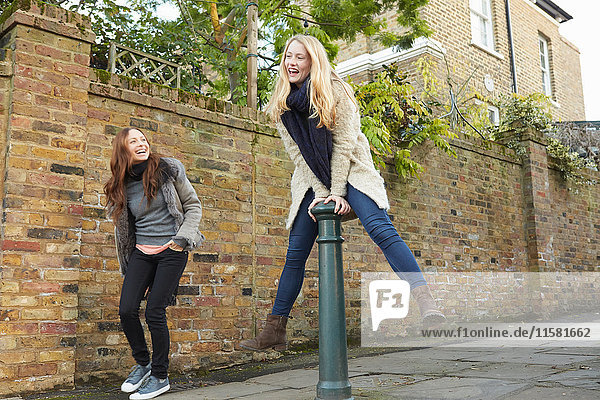 Junge Frau springt auf der Straße  während ein Freund zuschaut und lacht.