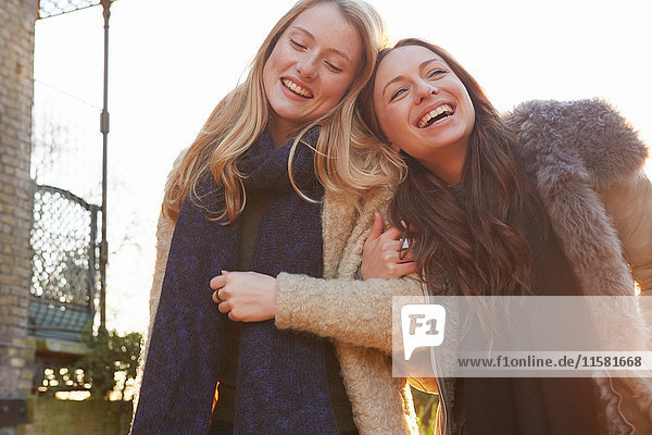 Zwei Freundinnen im Freien  Arm in Arm gehen  lachend