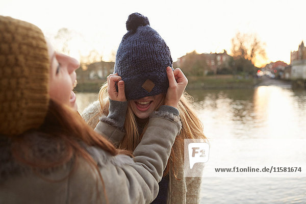 Junge Frau setzt Strickmütze auf Freund  Hut über den Augen  lachend