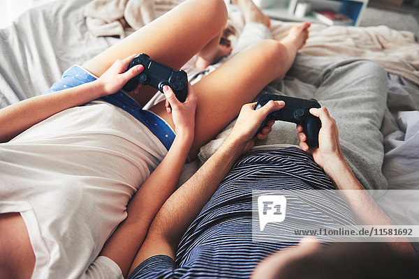 Couple relaxing on bed  holding computer controllers