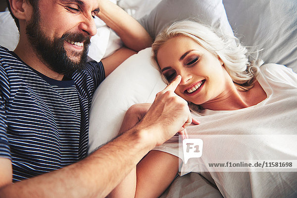 Couple lying in bed  fooling around  man poking woman's nose