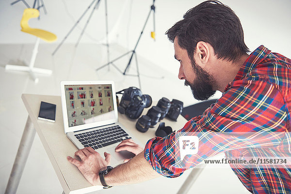Male photographer reviewing photo shoot on laptop in studio