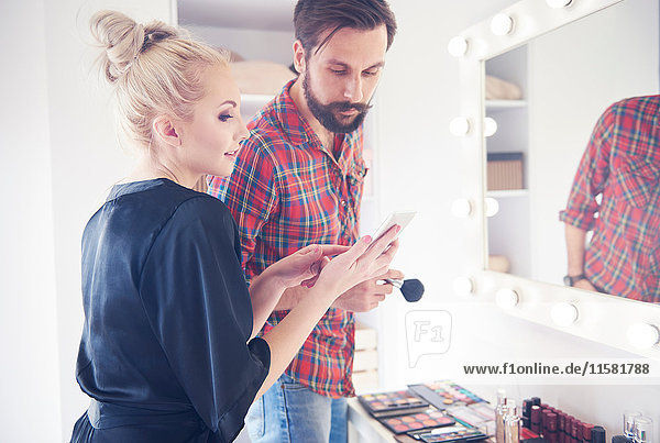 Männlicher Make-up-Künstler und Model schauen sich vor dem Fotoshooting ein Smartphone an