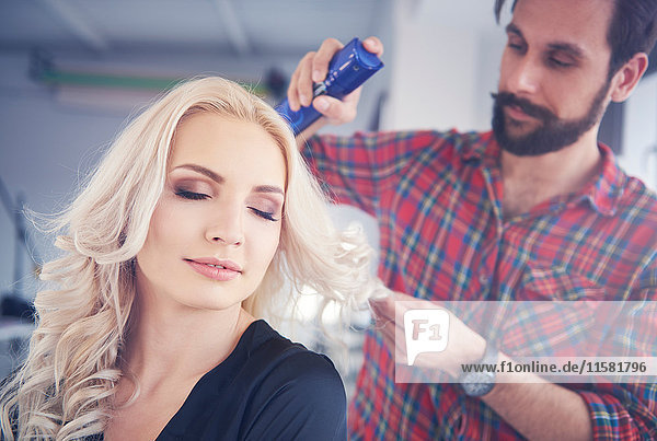 Männlicher Friseur versprüht Haarspray an Modell für Fotoshooting