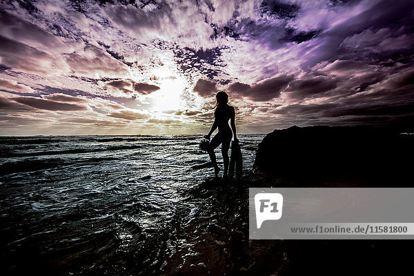 Silhouettierte sexy Frau  die auf Küstenfelsen am Wasser steht