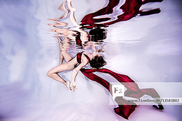 Unterwasseransicht einer balancierten Frau mit fließenden roten Textilien