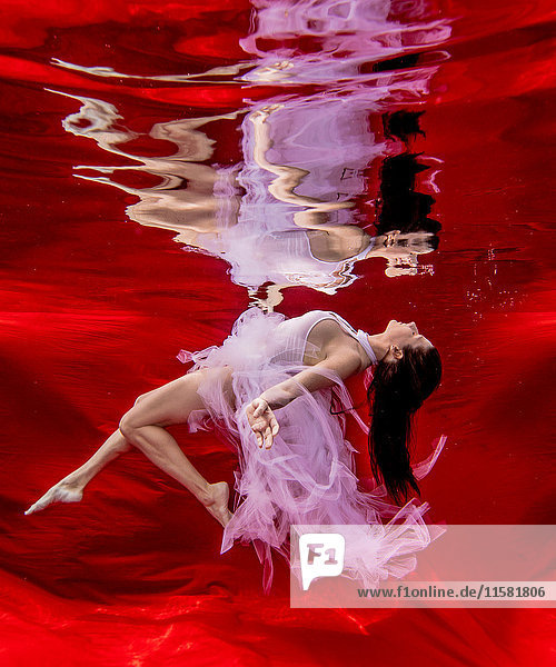 Unterwasseransicht einer balancierten Frau mit fließendem rosa Kleid vor rotem Hintergrund
