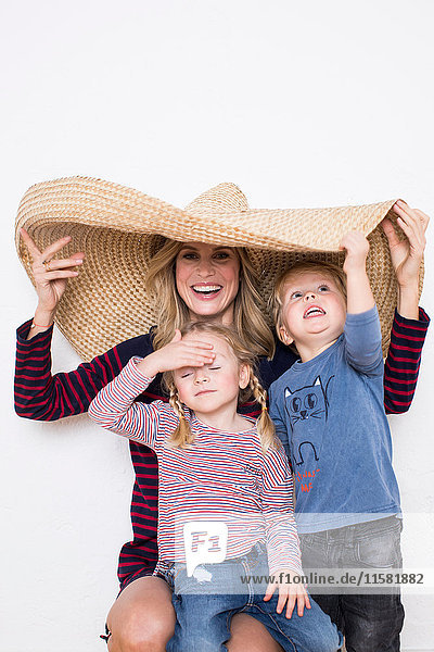 Frau  die einen Sombrero trägt und sowohl sich selbst als auch zwei Kinder abschirmt